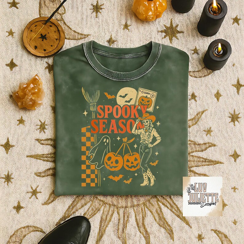 May include: Green crew neck sweatshirt with an orange and white graphic that says "Spooky Season". The graphic includes a witch's broom, a ghost, pumpkins, bats, and a cowgirl. The sweatshirt has a vintage, washed look.