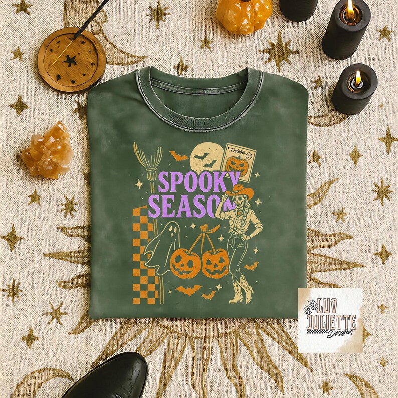 May include: Green crew neck sweatshirt with a Halloween-themed graphic. The design includes the words "Spooky Season", a ghost, pumpkins, bats, and a cowgirl. The sweatshirt has a vintage, washed look.