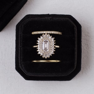 May include: Three gold rings with diamonds in a black velvet ring box. The center ring features a large rectangular diamond surrounded by smaller diamonds.