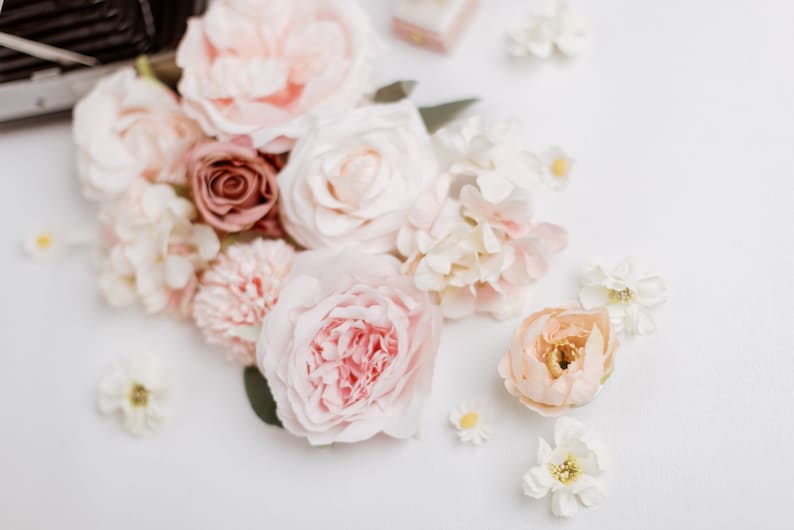May include: An assortment of soft, pastel-colored flowers, including roses, peonies, and smaller blossoms, arranged on a white surface. The color palette includes shades of pink, peach, cream, and a touch of burgundy, creating a delicate and romantic aesthetic.