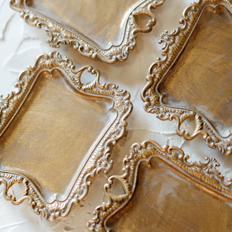 May include: Four ornate gold-colored metal trays with intricate designs. The trays are arranged in a staggered pattern, with the top tray partially obscured by the tray below it.