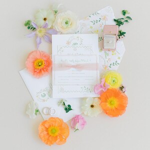Puede incluir: Un conjunto de invitaciones de boda con detalles florales, que incluye un anillo en una caja rosa, rodeado de flores coloridas. La invitaci&oacute;n tiene una cinta y el texto "Happily ever after, March 1".
