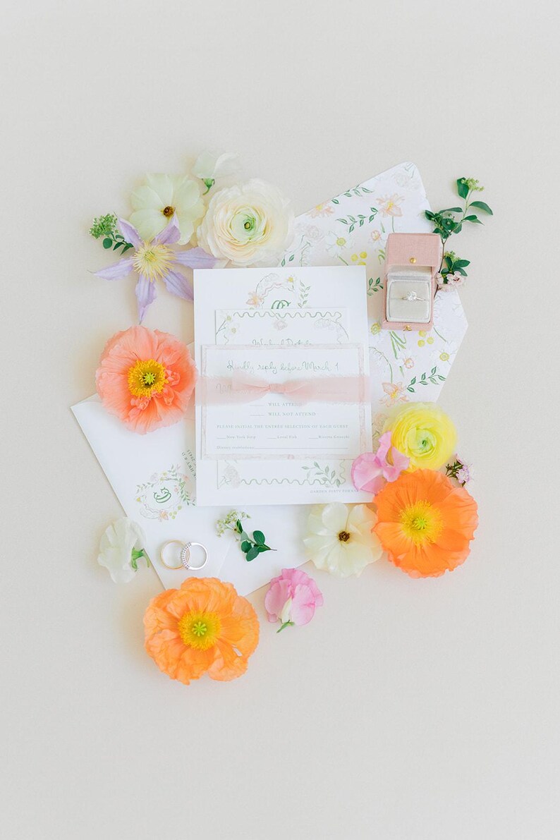 Puede incluir: Un conjunto de invitaciones de boda con detalles florales, que incluye un anillo en una caja rosa, rodeado de flores coloridas. La invitaci&oacute;n tiene una cinta y el texto "Happily ever after, March 1".