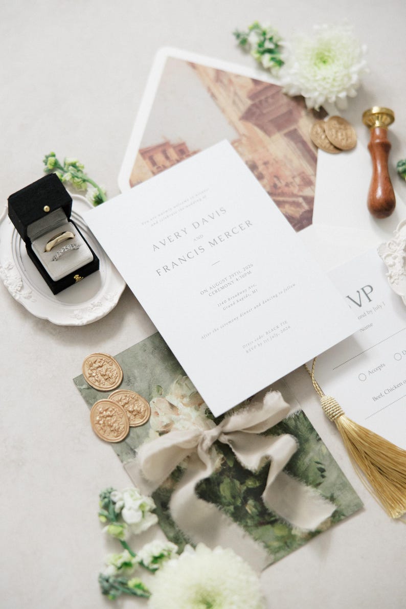 Puede incluir: Conjunto de papeler&iacute;a de boda con una invitaci&oacute;n formal con los nombres "AVERY DAVIS y FRANCIS MERCER". Incluye una caja negra para anillos con dos anillos, sellos de cera dorados y una borla dorada. El conjunto tiene una paleta de colores neutros.