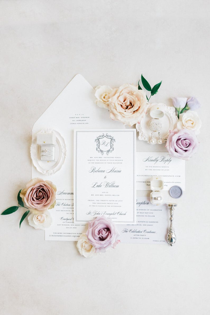 Puede incluir: Elegante conjunto de invitaciones de boda con una tarjeta de invitaci&oacute;n central y detalles florales. El dise&ntilde;o incluye un sobre blanco, una tarjeta de confirmaci&oacute;n y una tarjeta de detalles, complementado con anillos en una caja y un sello de cera. Rosas rosas y lavanda suaves a&ntilde;aden un toque rom&aacute;ntico.