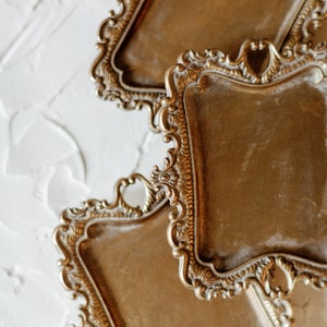 May include: Three ornate gold-toned metal trays with intricate designs. The trays are stacked on top of each other, with the top tray partially obscuring the tray below it.