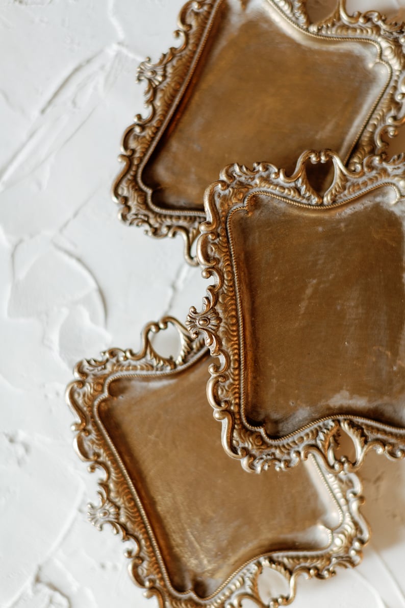 May include: Three ornate gold-toned metal trays with intricate designs. The trays are stacked on top of each other, with the top tray partially obscuring the tray below it.