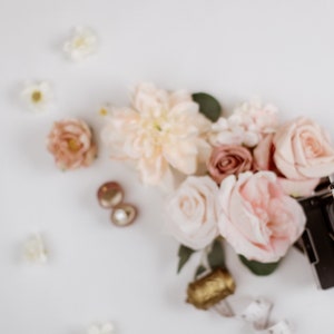 May include: A flat lay featuring a vintage Polaroid camera, blush and peach-colored roses, and small white flowers. Gold-toned earrings and a decorative gold object are also present, creating a romantic and artistic composition.