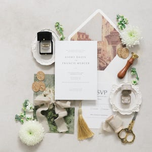 Puede incluir: Conjunto de papeler&iacute;a de boda con anillos, flores y detalles dorados. La invitaci&oacute;n dice "AVERY DAVIS y FRANCIS MERCER". Incluye una borla dorada, tijeras y sellos de cera.
