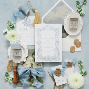Puede incluir: Un elegante conjunto de papeler&iacute;a de boda con detalles en azul claro. Incluye tarjetas de invitaci&oacute;n, tarjetas de confirmaci&oacute;n de asistencia, sobres, anillos en cajas, sellos de cera dorados, cinta azul, tijeras y adornos florales. La invitaci&oacute;n dice "Alexander y Rosalee, 16 de mayo de 2016."
