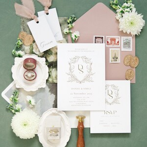 Puede incluir: Conjunto de papeler&iacute;a de boda con un sobre rosa rubor, sellos e invitaciones. La invitaci&oacute;n presenta un dise&ntilde;o de corona dorada con los nombres "Daniel & Sibble" y la fecha "22 de noviembre de 2025". Incluye anillos, etiquetas y sellos de cera.
