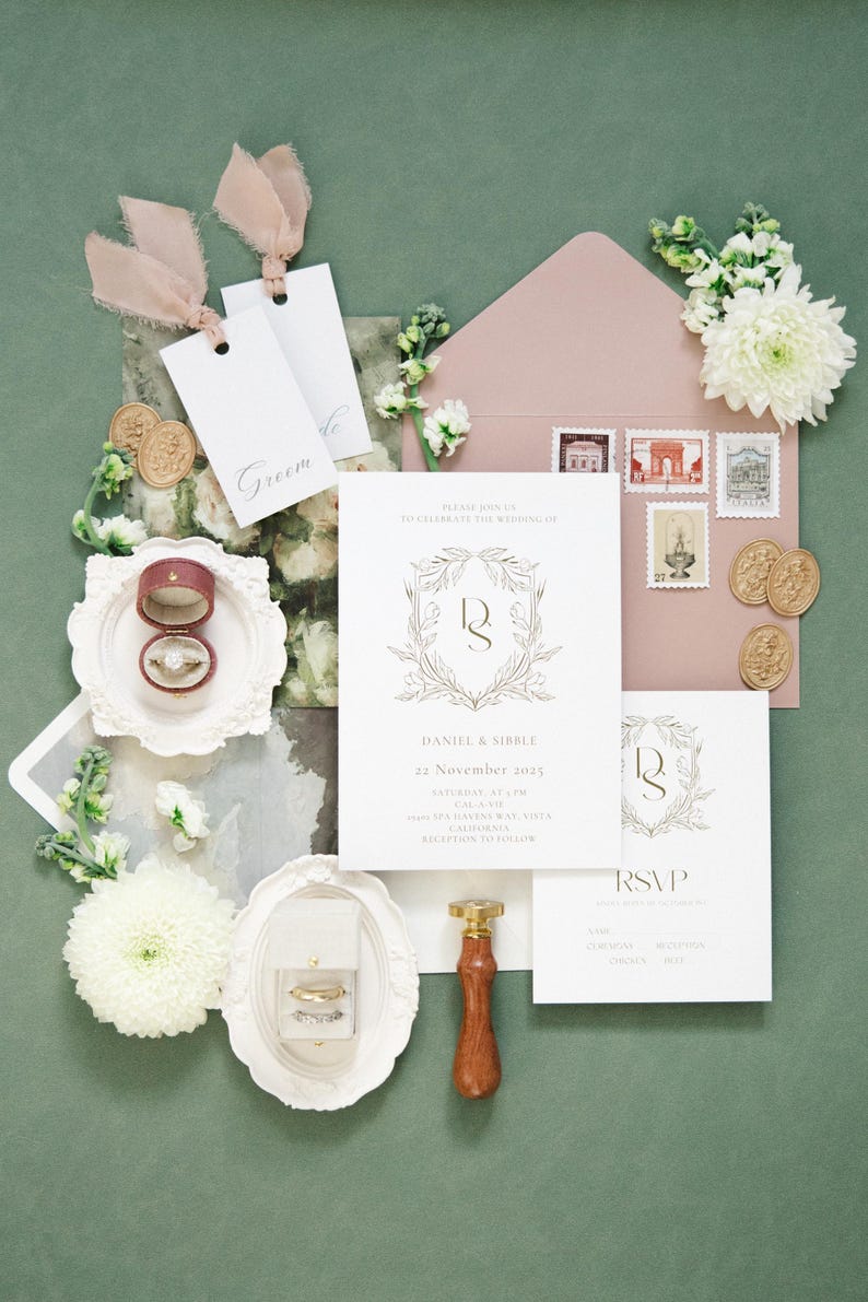 Puede incluir: Conjunto de papeler&iacute;a de boda con un sobre rosa rubor, sellos e invitaciones. La invitaci&oacute;n presenta un dise&ntilde;o de corona dorada con los nombres "Daniel & Sibble" y la fecha "22 de noviembre de 2025". Incluye anillos, etiquetas y sellos de cera.