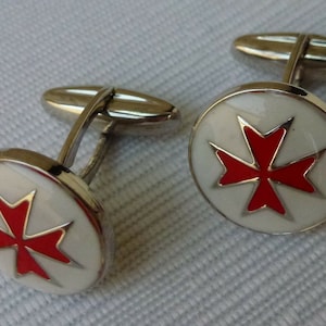 May include: A pair of silver cufflinks with a white enamel background and a red Maltese cross design.
