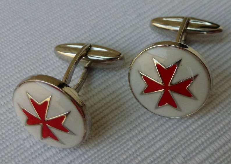 May include: A pair of silver cufflinks with a white enamel background and a red Maltese cross design.