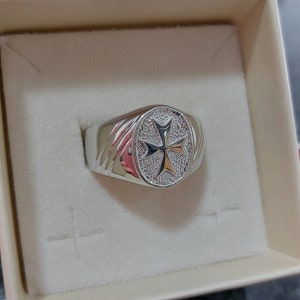 Könnte beinhalten: Ein silberner Ring mit einem erhabenen, ovalen Design, das ein Malteserkreuz mit einer strukturierten Oberfläche zeigt.