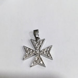 Könnte beinhalten: Ein silberner Anhänger in Form eines Malteserkreuzes, mit kleinen, klaren Steinen, die in das Metall eingefasst sind.