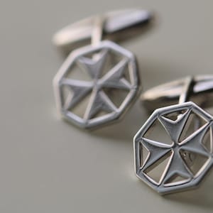 Puede incluir: Un par de gemelos de plata con un diseño de cruz de Malta.