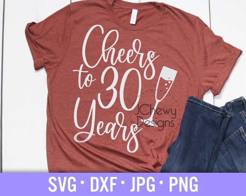May include: A red t-shirt with the text "Cheers to 30 Years" in white lettering. A white silhouette of a champagne flute is next to the text. The text "JChewy Designs" is in a circle below the text.