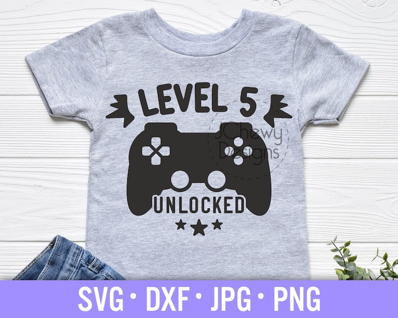 Op de afbeelding: Een grijs T-shirt met een zwarte videogamecontroller-afbeelding en de tekst "LEVEL 5 UNLOCKED" met drie sterren eronder.