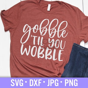 Puede incluir: Una camiseta de color óxido con el texto blanco "gobble 'til you wobble" en una fuente de escritura. La camiseta se combina con unos vaqueros azules doblados. La parte inferior de la imagen muestra los tipos de archivo: SVG, DXF, JPG y PNG.