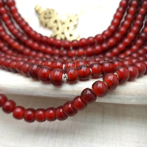 May include: A strand of deep red glass beads, each bead is round and slightly translucent. The beads are arranged in a circular pattern, creating a beautiful and elegant look.