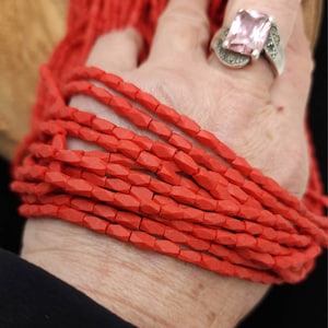 May include: A strand of bright red faceted beads, made of natural gemstone, in a hand. The beads are approximately 6mm in size.