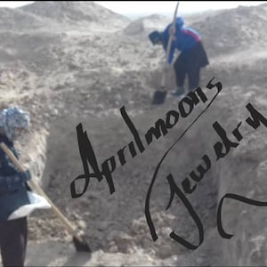 May include: Two people wearing winter clothing are digging in a dirt pit. The text "Aprilmoon's Jewelry" is written in black cursive on the dirt.