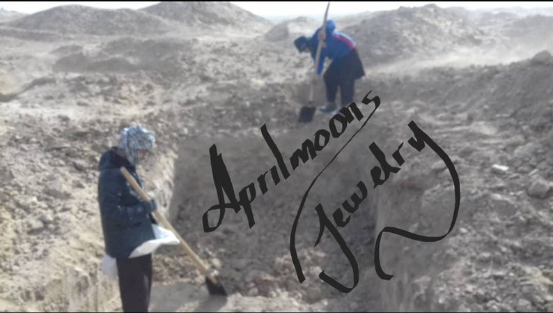 May include: Two people wearing winter clothing are digging in a dirt pit. The text "Aprilmoon's Jewelry" is written in black cursive on the dirt.