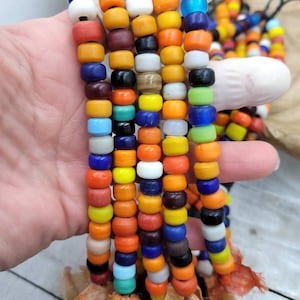 May include: A collection of colorful glass beads, strung on a cord, with a frayed fabric tassel at the bottom. The beads are a mix of orange, yellow, blue, green, and white.