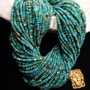 May include: A strand of turquoise beads, with a variety of shades of blue and green, and a gold pendant with a face design.