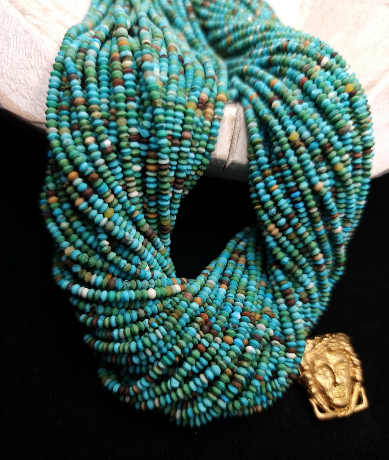 May include: A strand of turquoise beads, with a variety of shades of blue and green, and a gold pendant with a face design.