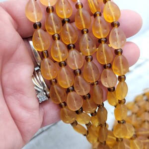 May include: A strand of amber glass beads with a teardrop shape. The beads have a frosted finish and are strung on a clear thread.