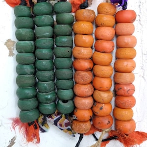May include: A strand of green and orange beads, each bead is round and has a slightly textured surface. The beads are strung on a cord and tied with fabric scraps.