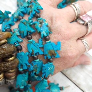 May include: A turquoise blue necklace with carved bird-shaped beads. The beads are strung on a brown cord with black beads interspersed between the turquoise beads.
