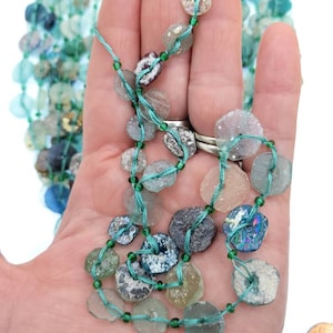 May include: A strand of turquoise and green glass beads, some with iridescent finishes, strung on a thin green thread.