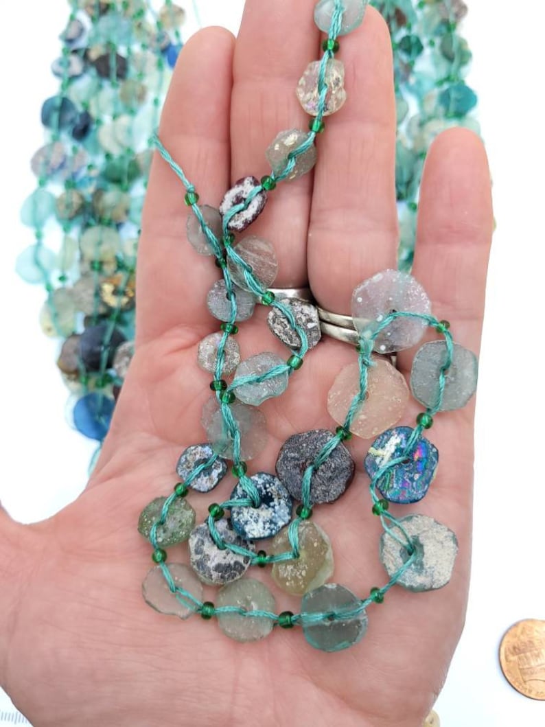 May include: A strand of turquoise and green glass beads, some with iridescent finishes, strung on a thin green thread.