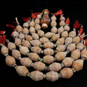 May include: A necklace featuring large, irregularly shaped, tan beads with red cross-hatch patterns. The beads are strung with smaller, colorful glass beads and red tassel accents. A decorative, multi-colored glass bead is at the top.