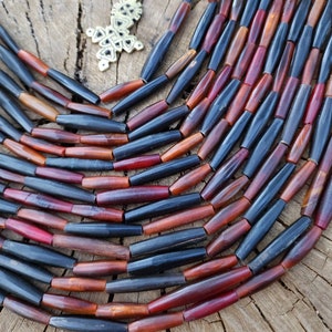 May include: A close-up of a necklace made of dark brown and red wooden beads. The beads are cylindrical and have a smooth, polished finish. The necklace is laid out on a wooden surface.