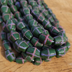 Pode incluir: Um fio de contas de vidro verde com padrões de cruz azuis e vermelhos. As contas estão empilhadas e dispostas em uma pilha.