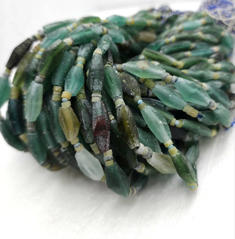May include: A strand of green, blue, and brown glass beads. The beads are irregular in shape and have a frosted finish.