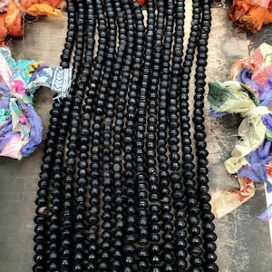 Puede incluir: Un conjunto de cuentas de oración negras, también conocidas como cuentas mala, con borlas negras. Las cuentas están enhebradas en un cordón negro y están dispuestas en una línea vertical. Las cuentas están hechas de un material liso y pulido.