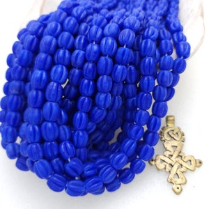 Pode incluir: Um fio de contas de vidro azul brilhante com uma superfície texturizada e estriada. As contas são enfiadas em um fio longo e contínuo.