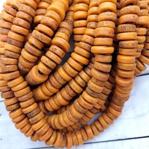 May include: A close-up of a pile of orange and brown round beads. The beads are made of natural materials and have a rustic, aged look.