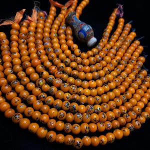 May include: A strand of orange glass beads with black and white speckles. The beads are strung on a cord and are arranged in a semi-circle.