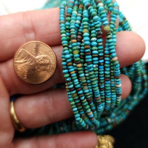 May include: A strand of turquoise beads, approximately 2mm in diameter, with a variety of colors and patterns. The beads are shown next to a US penny for scale.