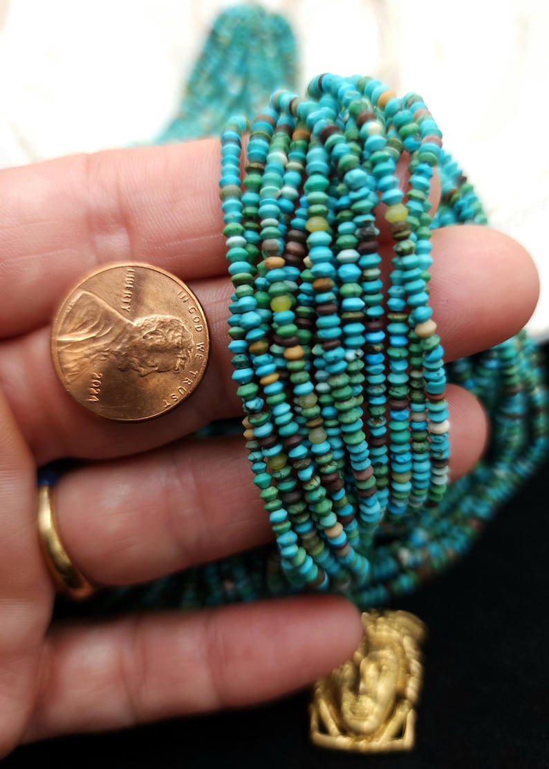 May include: A strand of turquoise beads, approximately 2mm in diameter, with a variety of colors and patterns. The beads are shown next to a US penny for scale.