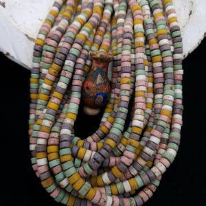 May include: A collection of colorful, round beads in shades of yellow, pink, green, purple, and white. A small, decorative vase with a painted design is nestled among the beads. The beads are strung together, creating a layered effect.