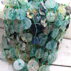 May include: A strand of turquoise and green glass beads, some with a frosted finish, strung on a thin green cord. The beads are irregular in shape and size, and some have a slightly iridescent sheen.