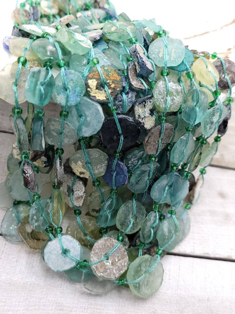 May include: A strand of turquoise and green glass beads, some with a frosted finish, strung on a thin green cord. The beads are irregular in shape and size, and some have a slightly iridescent sheen.