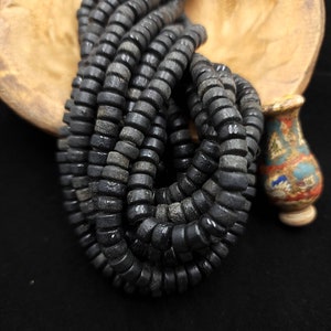 Pode incluir: Um fio de contas de madeira redondas e pretas. As contas são empilhadas e enroladas juntas, criando um visual texturizado e orgânico.